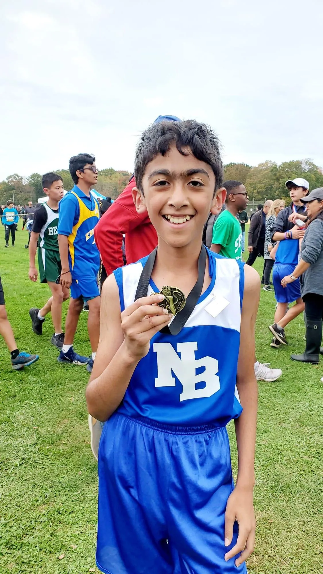 A younger Anish smiling and holding up a medal in a North Brunswick singlet