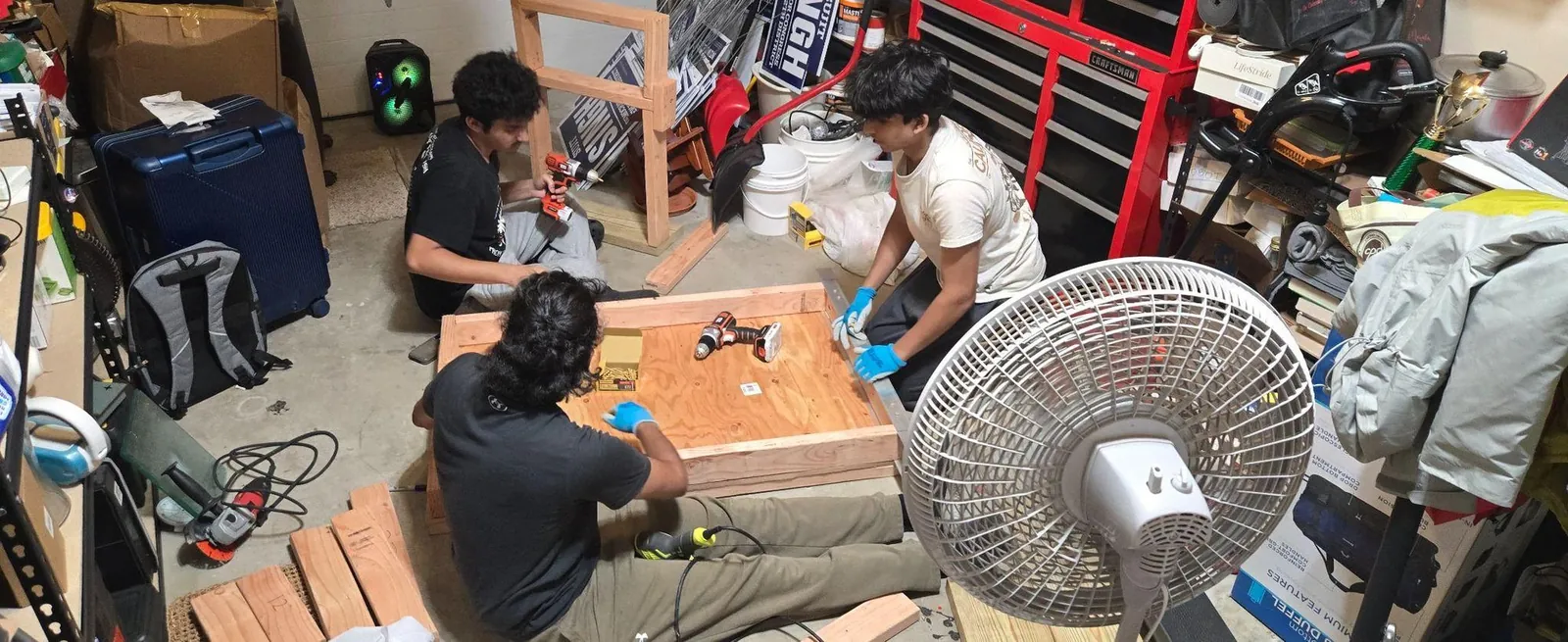 Three people assembling the floor pan in a garage