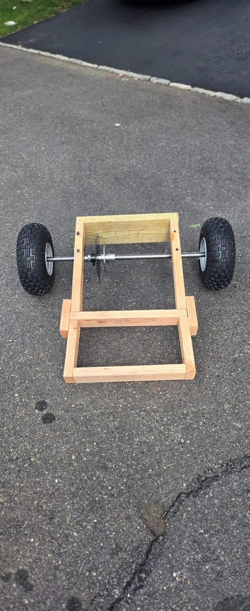 Rear wooden frame with axle, sprocket and two wheels on a driveway