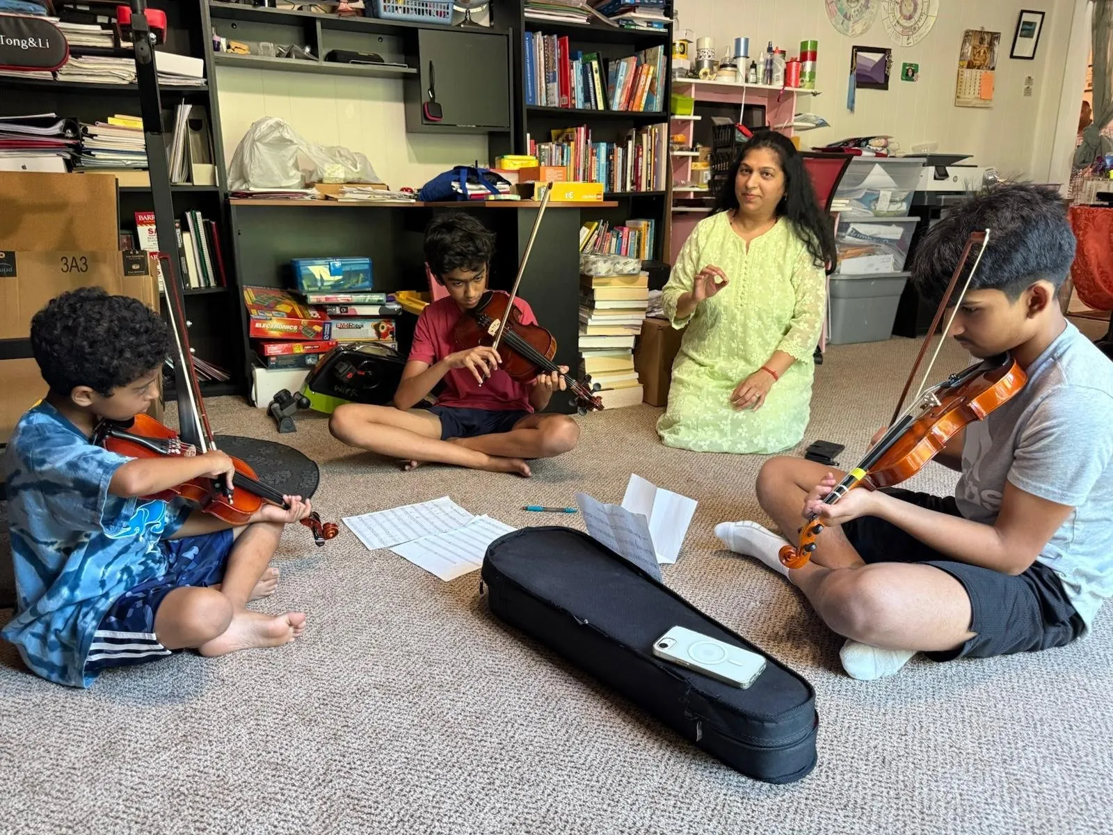 Young musicians practicing violin seated on a carpet with an adult instructor