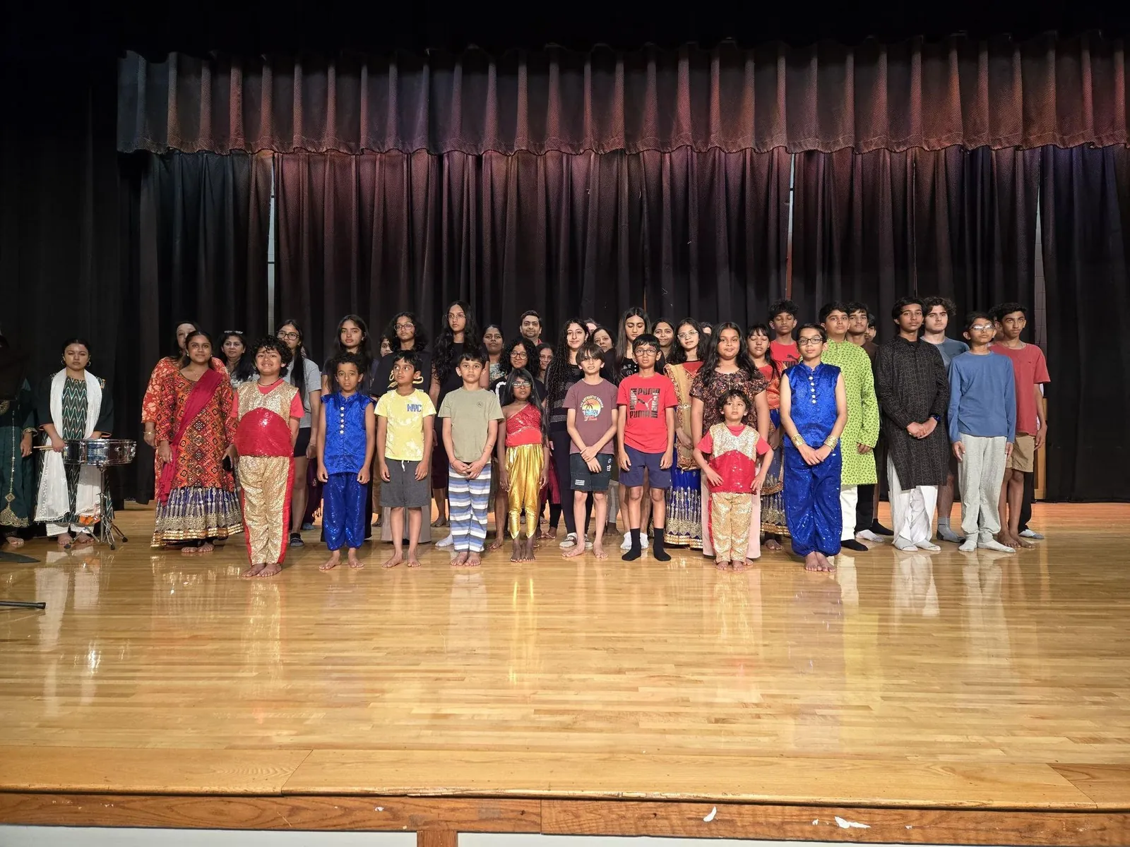 Large group of children and teens in traditional and casual clothes standing on a school stage