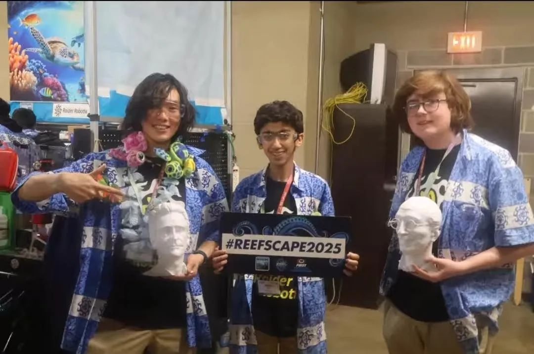 Anish holding a #REEFSCAPE2025 sign between two teammates in the pit