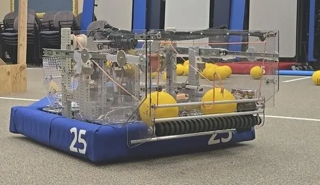 Robot with blue bumpers numbered 25 and yellow foam balls on a practice field