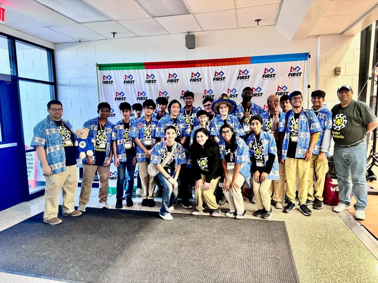 Raider Robotix team members in matching blue shirts posing in front of a FIRST Mid-Atlantic backdrop